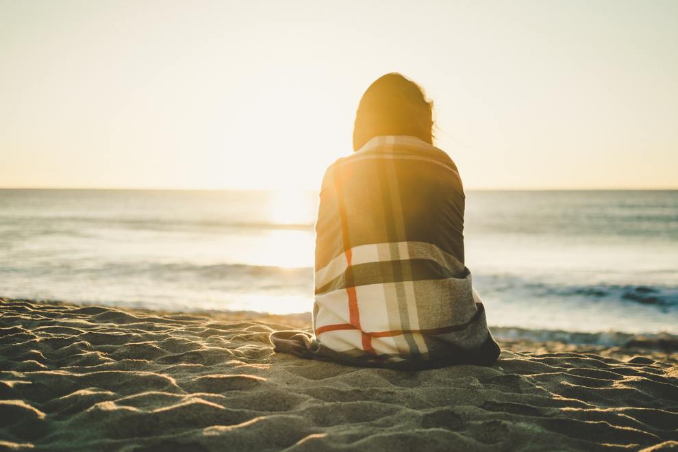 woman on beach in blanket looking at water