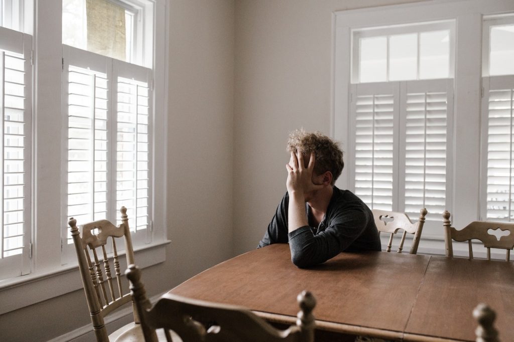 man covering face with hand sitting at dining room table