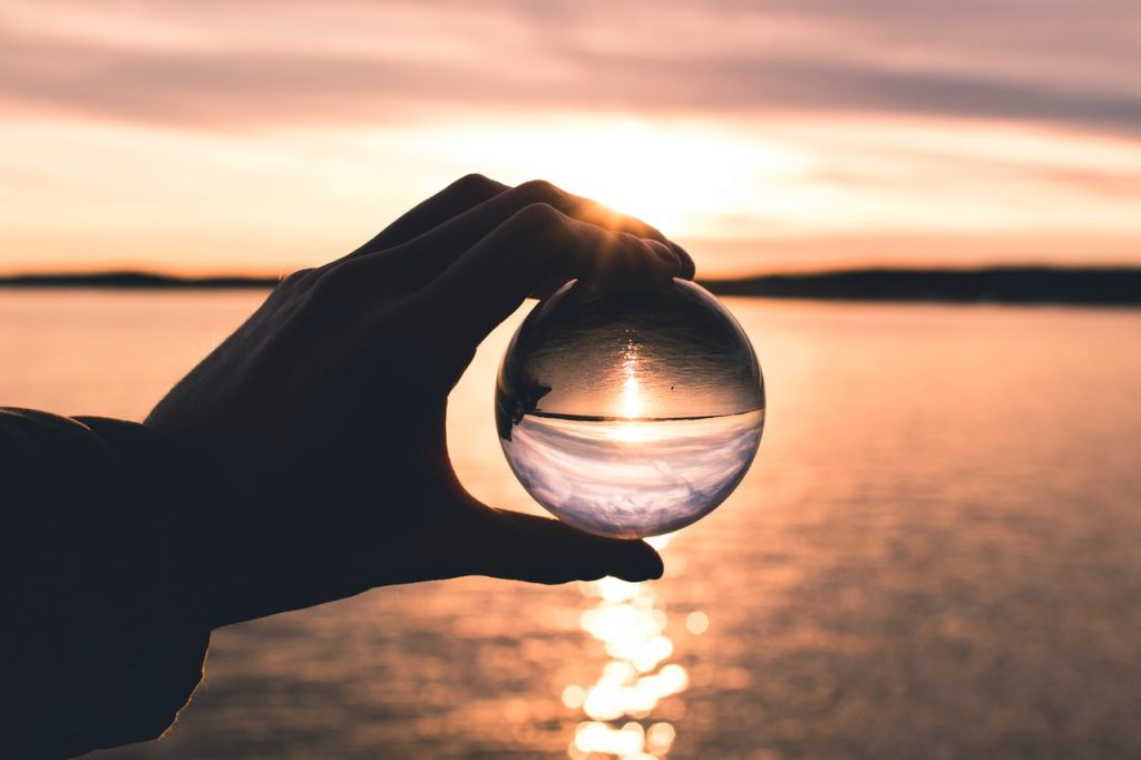 hand holding glass ball with reflection of water and sky
