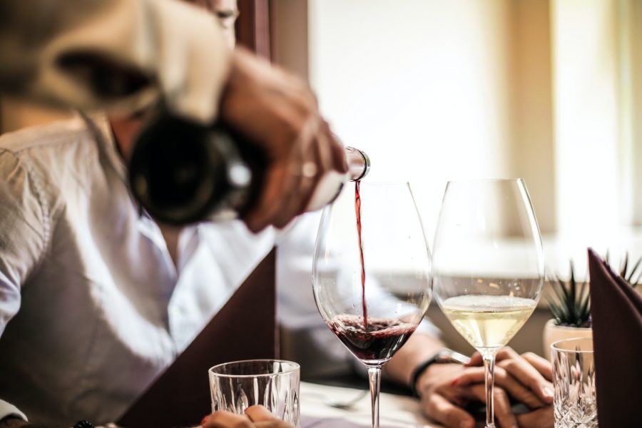 man pouring red wine into glass