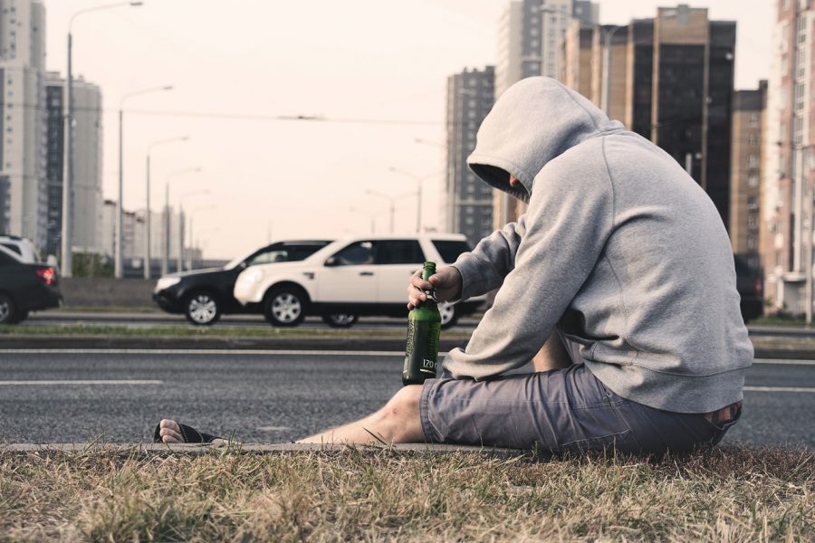 man in hoodie sitting on edge of road with bottle